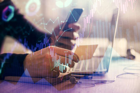 Double exposure of mans hands holding and using a phone and financial graph drawing. Analysis...