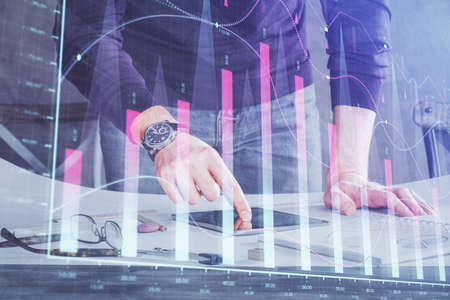 Double exposure of mans hands holding and using a digital device and forex graph drawing. Financial...