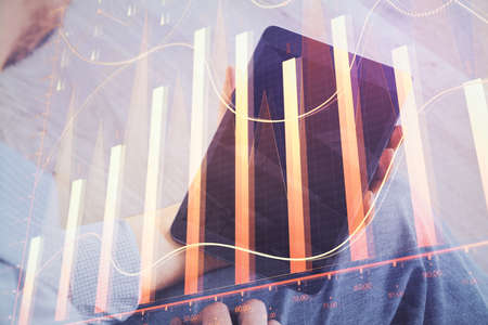 Double exposure of mans hands holding and using a digital device and forex graph drawing. Financial...
