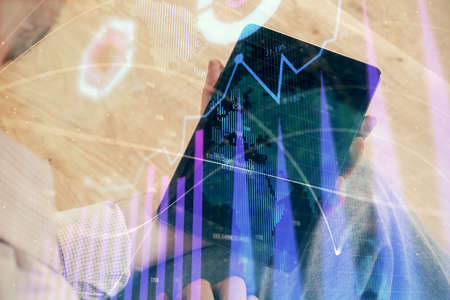 Double exposure of mans hands holding and using a digital device and forex graph drawing. Financial...