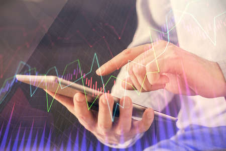 Double exposure of mans hands holding and using a digital device and forex graph drawing. Financial...