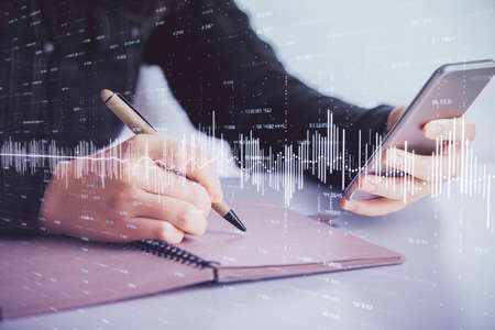 Double exposure of forex graph sketch hologram and woman holding and using a mobile device. Stock...