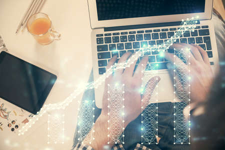 Double exposure of mans hands typing over laptop keyboard and forex chart hologram drawing. Top...
