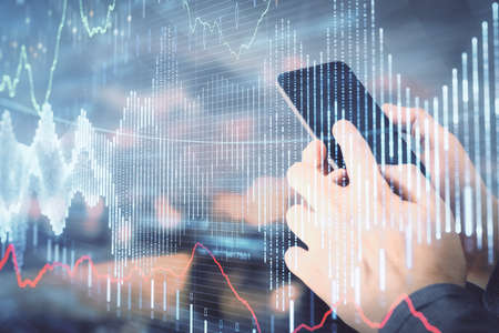 Double exposure of mans hands holding and using a digital device and forex graph drawing. Financial...