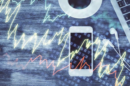 Double exposure of forex chart hologram over desktop with phone. Top view. Mobile trade platform...