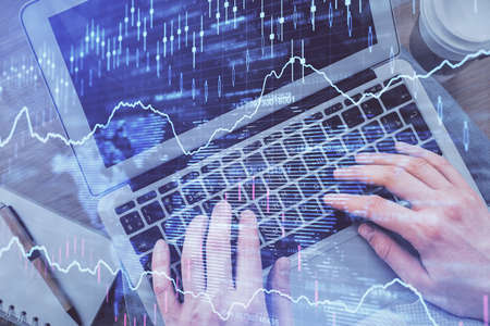 Double exposure of man's hands typing over computer keyboard and forex graph hologram drawing. Top...