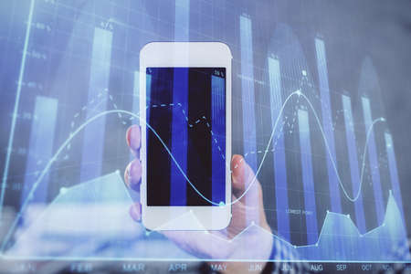 Double exposure of man's hands holding and using a digital device and forex graph drawing. Financial...