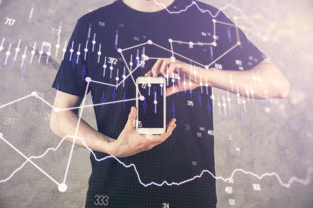 Double exposure of man's hands holding and using a digital device and forex graph drawing. Financial...
