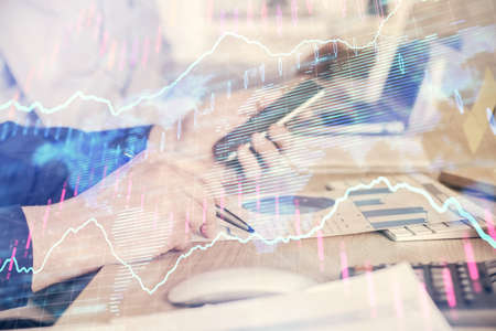 Double exposure of man's hands holding and using a digital device and forex graph drawing. Financial...