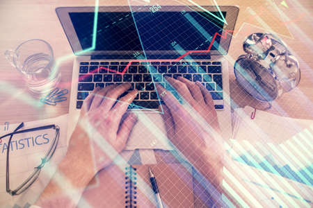 Double exposure of man's hands typing over laptop keyboard and forex chart hologram drawing. Top...