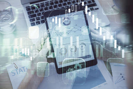 Double exposure of man's hands holding and using a digital device and forex graph drawing. Financial...
