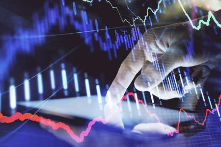 Double exposure of man's hands holding and using a digital device and forex graph drawing. Financial...