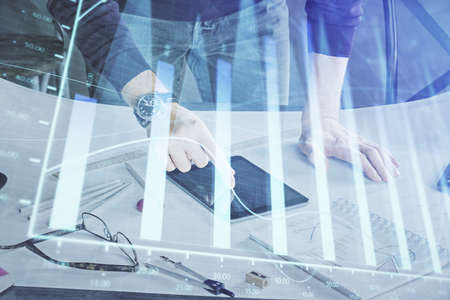 Double exposure of man's hands holding and using a digital device and forex graph drawing. Financial...