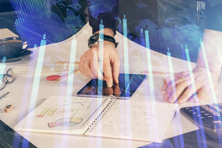 Double exposure of man's hands holding and using a digital device and forex graph drawing. Financial...