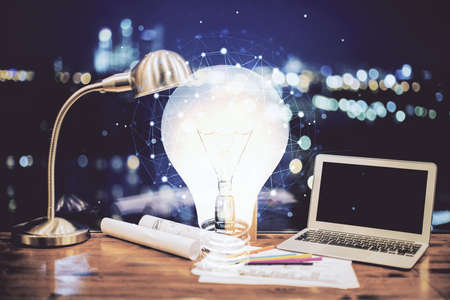 Computer on desktop in office with bulb icon hologram. Double exposure. Concept of idea.