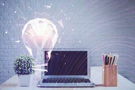Computer on desktop in office with bulb icon hologram. Double exposure. Concept of idea.