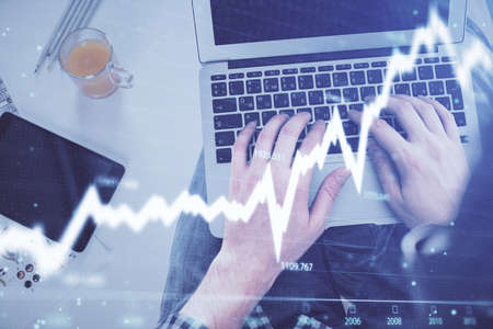 Double exposure of man's hands typing over laptop keyboard and forex chart hologram drawing. Top...