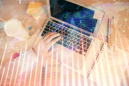 Double exposure of man's hands typing over computer keyboard and forex graph hologram drawing. Top...