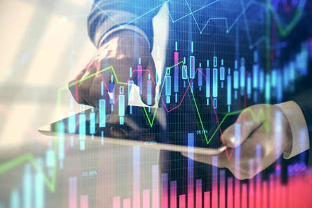 Double exposure of man's hands holding and using a digital device and forex graph drawing. Financial...