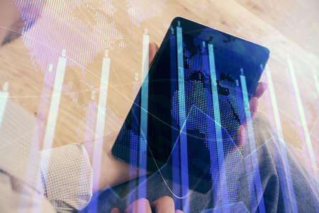 Double exposure of man's hands holding and using a digital device and forex graph drawing. Financial...