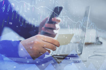 Double exposure of man's hands holding and using a phone and financial graph drawing. Analysis...