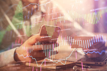 Double exposure of man's hands holding and using a phone and financial graph drawing. Analysis...