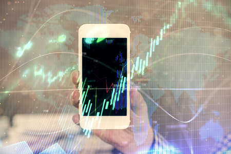 Double exposure of man's hands holding and using a digital device and forex graph drawing. Financial...