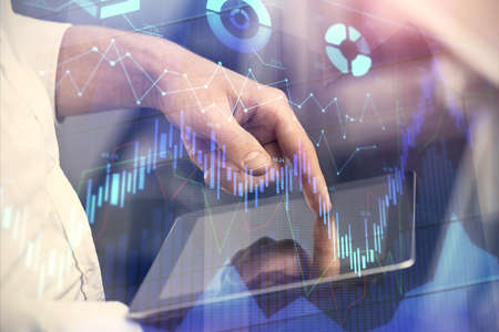 Double exposure of man's hands holding and using a digital device and forex graph drawing. Financial...