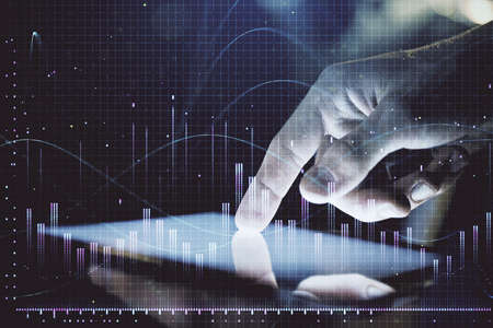 Double exposure of man's hands holding and using a digital device and forex graph drawing. Financial...