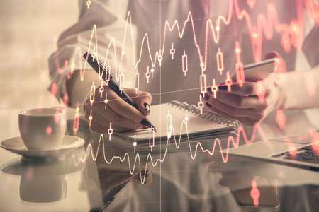 Double exposure of financial graph sketch hologram and woman holding and using a mobile device....