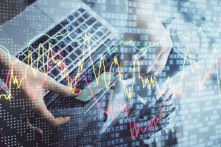 Double exposure of businesswoman hands typing on computer and financial graph hologram drawing....