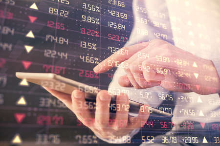 Double exposure of man's hands holding and using a digital device and forex graph drawing. Financial...
