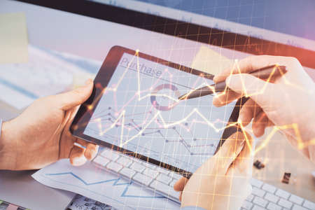Double exposure of man's hands holding and using a phone and financial chart drawing. Market...