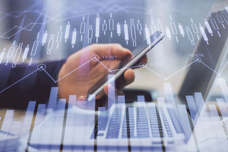 Double exposure of man's hands holding and using a phone and financial graph drawing. Analysis...