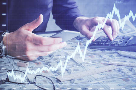 Double exposure of man's hands holding and using a digital device and forex graph drawing. Financial...