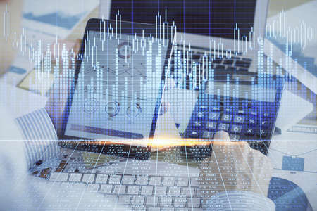 Double exposure of man's hands holding and using a digital device and forex graph drawing. Financial...