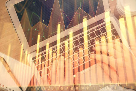Double exposure of man's hands typing over computer keyboard and forex graph hologram drawing. Top...