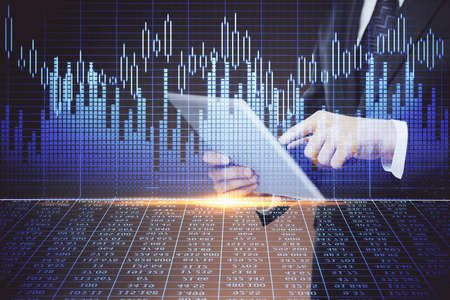 Double exposure of man's hands holding and using a digital device and forex graph drawing. Financial...