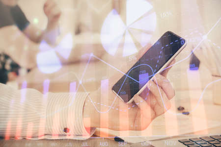 Double exposure of man's hands holding and using a digital device and forex graph drawing. Financial...