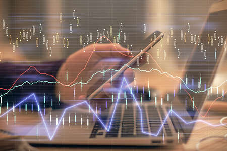 Double exposure of man's hands holding and using a phone and financial graph drawing. Analysis...