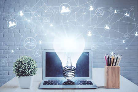 Computer on desktop in office with bulb icon hologram. Double exposure. Concept of idea.