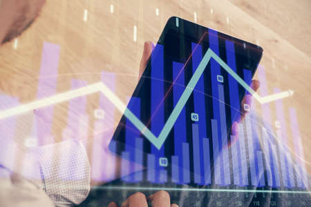 Double exposure of mans hands holding and using a digital device and forex graph drawing. Financial...