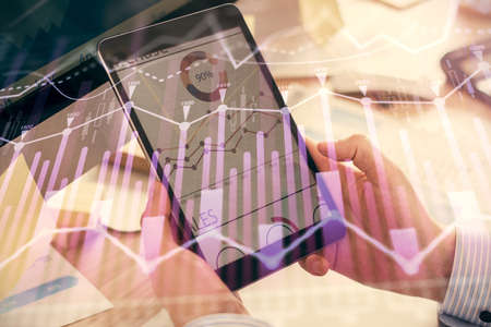 Double exposure of mans hands holding and using a phone and financial graph drawing. Analysis...