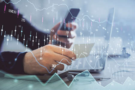 Double exposure of mans hands holding and using a phone and financial graph drawing. Analysis...