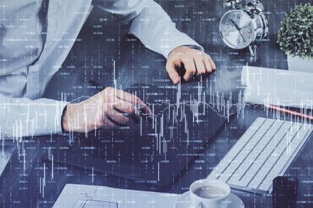 Double exposure of mans hands holding and using a phone and financial graph drawing. Analysis...