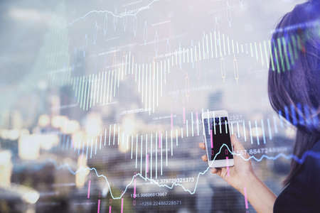 Double exposure of forex chart sketch hologram and woman holding and using a mobile device. Stock...