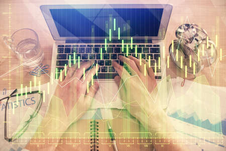 Double exposure of mans hands typing over laptop keyboard and forex chart hologram drawing. Top...