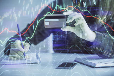 Double exposure of woman on-line shopping holding a credit card and financial graph drawing. Stock...