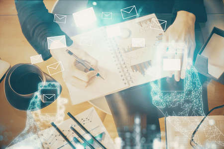 E-mail envelop theme hologram over hands taking notes background. Concept of electronic mail. Double...