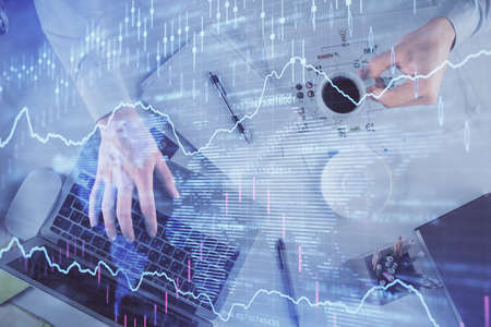 Multi exposure of mans hands typing over computer keyboard and forex graph hologram drawing. Top...